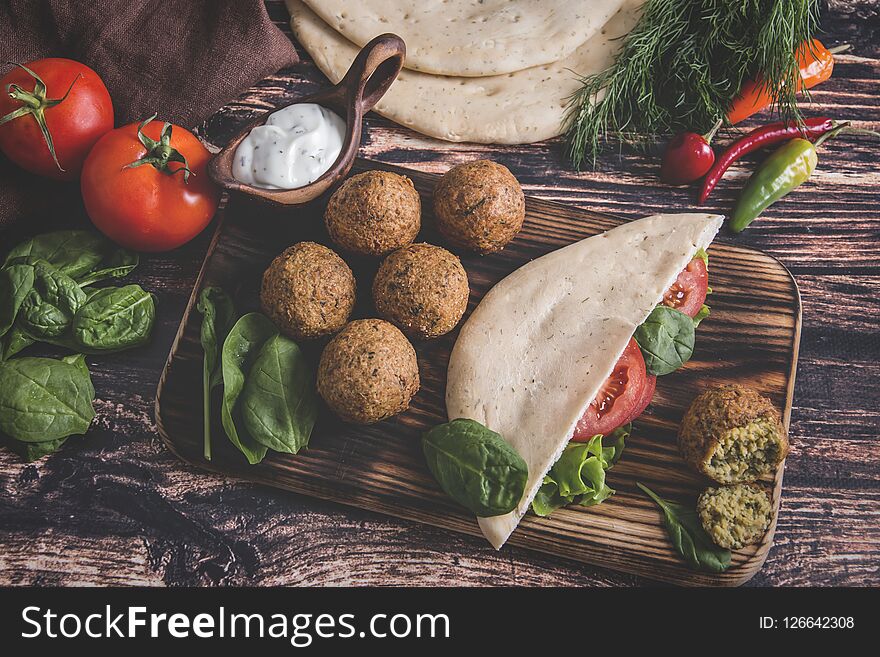 Falafel, fresh vegetables ,sauce and pita bread on wooden table