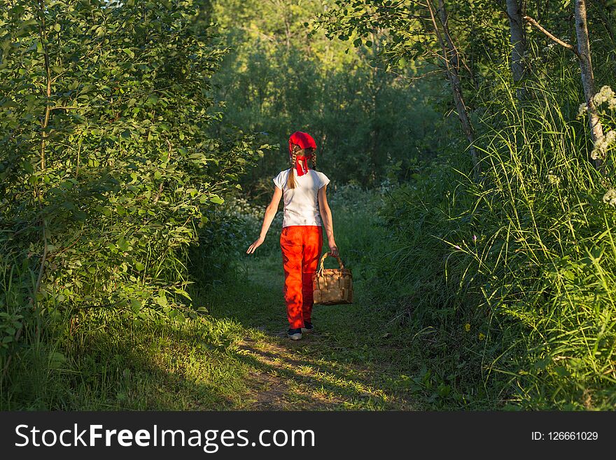 Young girl walking on a path through green woods carrying a basket