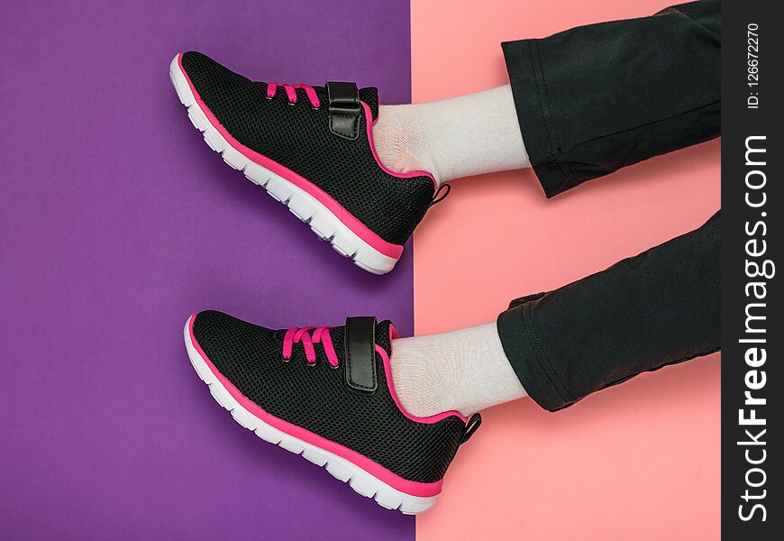 The girl`s legs in sweatpants and bright sneakers on a background of two colors. Colorful sports shoes.