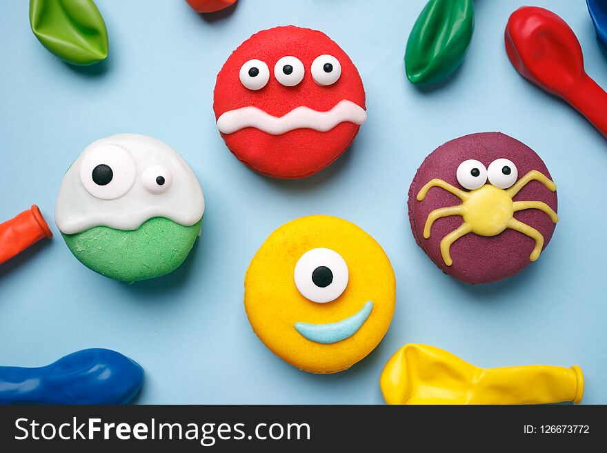 Heloween dessert: funny monsters made of biscuits macaroon with icing and candy eyes close-up on the table. horizontal, party concept