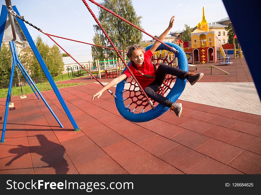Happy smiling girl swinging on a swing with closed eyes and arms outstretched at playground
