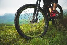Close-up Of A Mountain Bike Wheel In The Mountains On The Green Grass And Foot Of A Rider Stock Photos