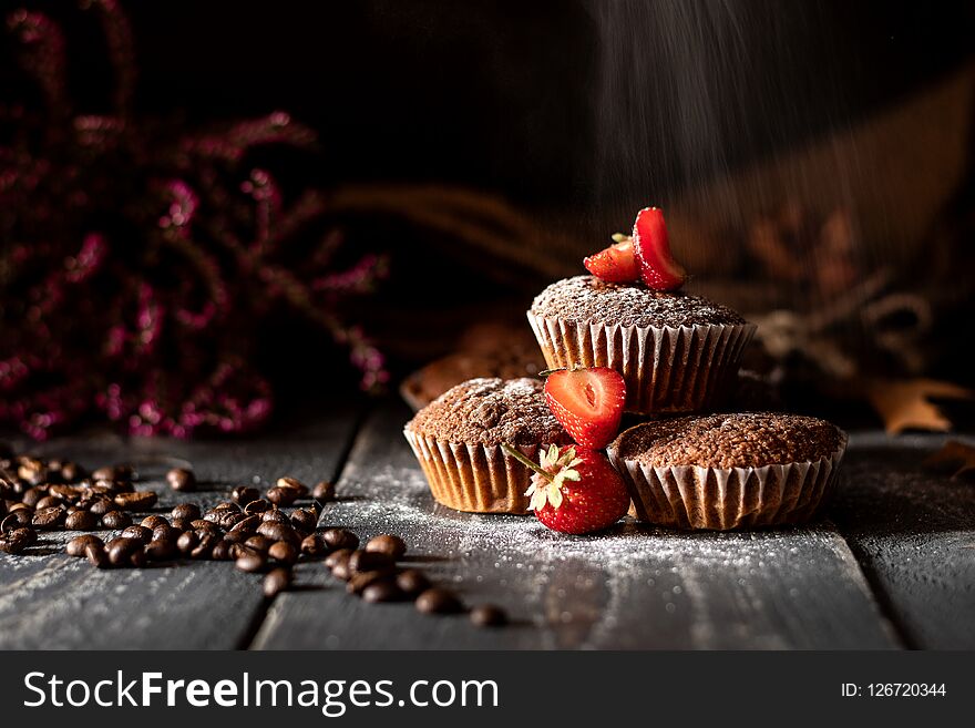 Sugar falling on muffins with strawberries laid on a jute bag with coffee beans and pink heather in the background. Sugar falling on muffins with strawberries laid on a jute bag with coffee beans and pink heather in the background.