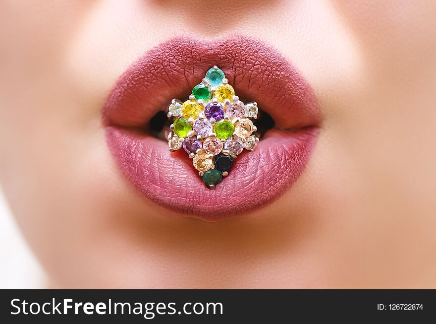 Close-up of beautiful woman`s lips with dark purple makeup holding silver ring with color gems.