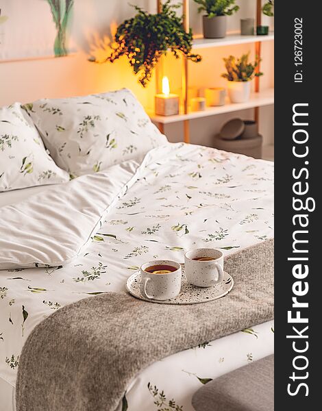 A mood created by a night lamp standing beside a bed dressed in green plants on white pattern linen and pillows in a natural style
