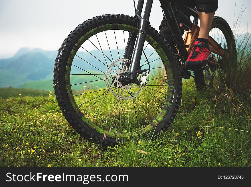 Close-up of a mountain bike wheel in the mountains on the green grass and foot of a rider.