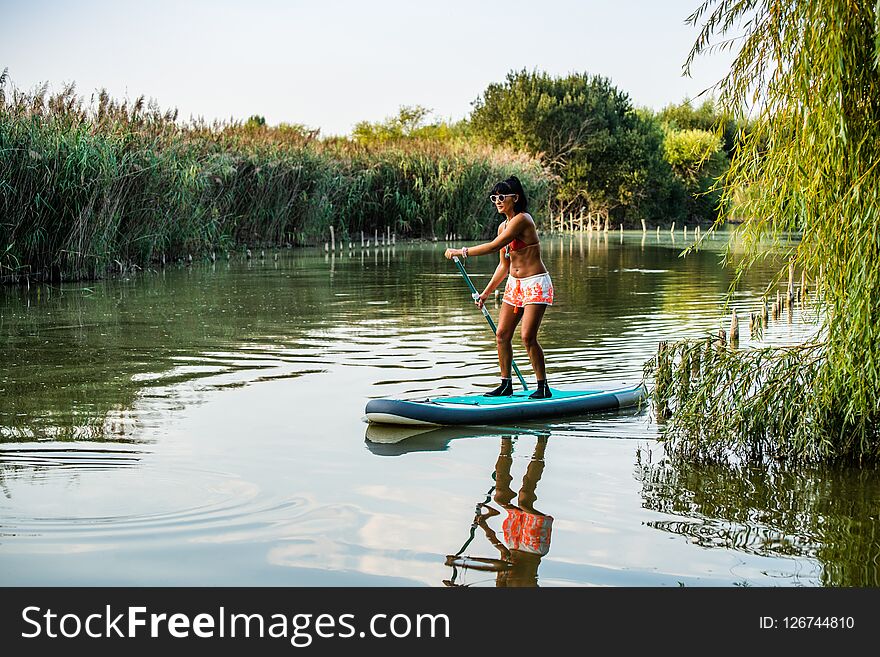 Woman stand up paddleboarding on lake. Young girl doing watersport on lake. Female tourist in swimwear during summer vacation.