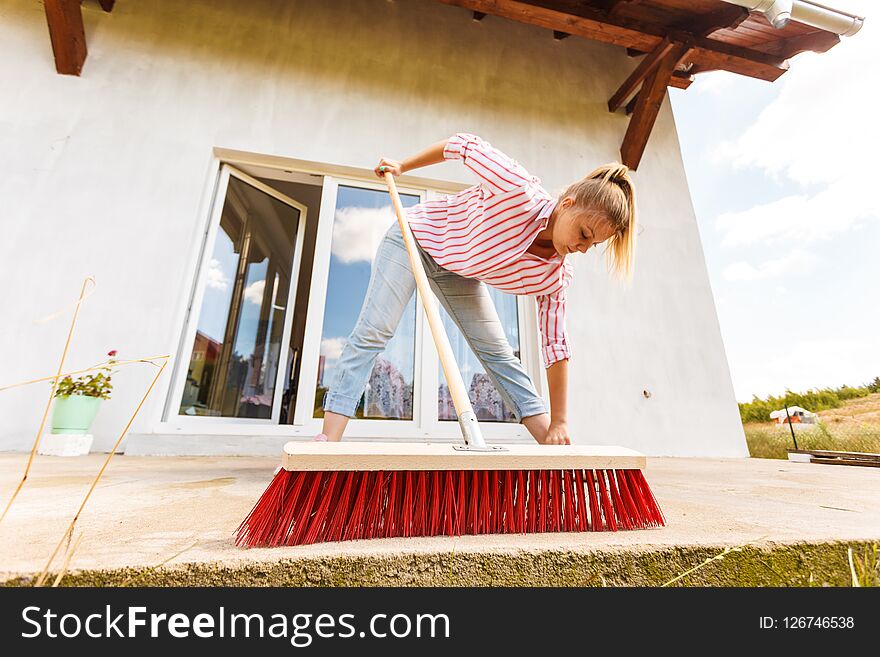 Woman cleaning patio using brush broom