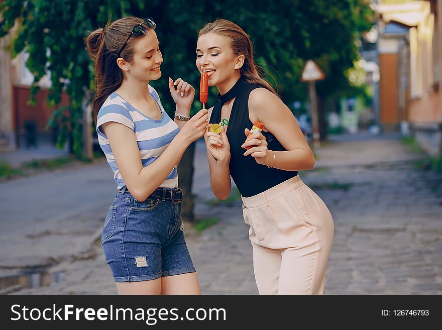 Two beautiful stylishly dressed girls walking around the summer city with ice cream and bubbles. Two beautiful stylishly dressed girls walking around the summer city with ice cream and bubbles