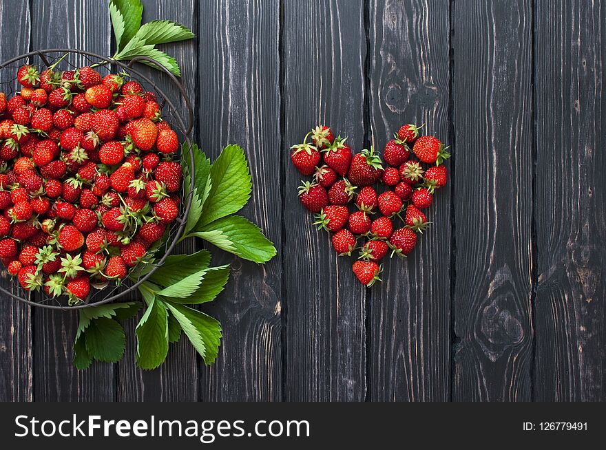 Fresh red strawberry in a bowl on a dark rustic wooden background, top view with copy space.
