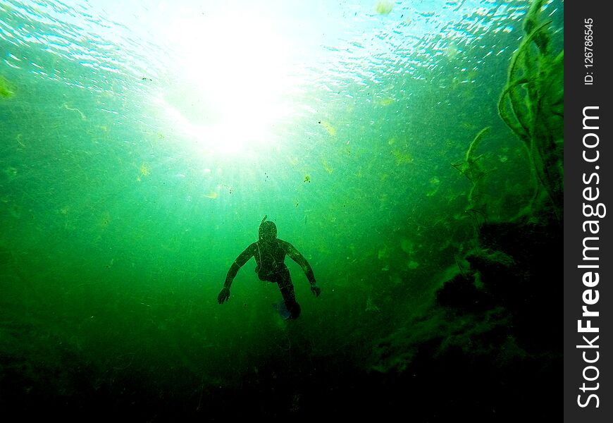 Freediver descending into a sinkhole with a high algae content, in front of a setting sun Limestone Coast, South Australia. Freediver descending into a sinkhole with a high algae content, in front of a setting sun Limestone Coast, South Australia.