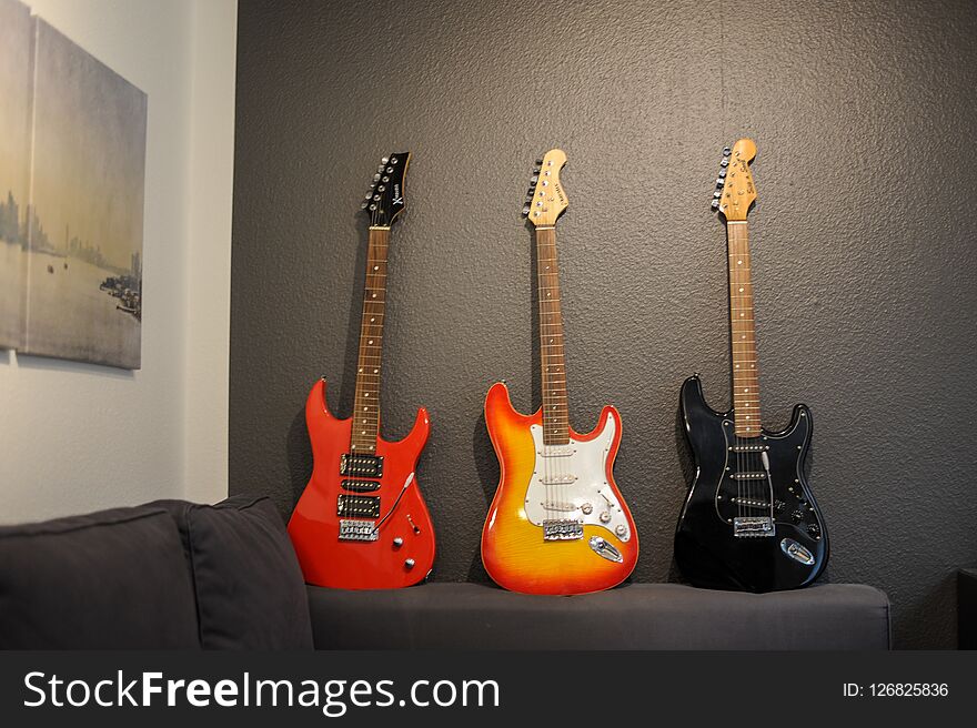 Three electric guitars of different colors on the couch