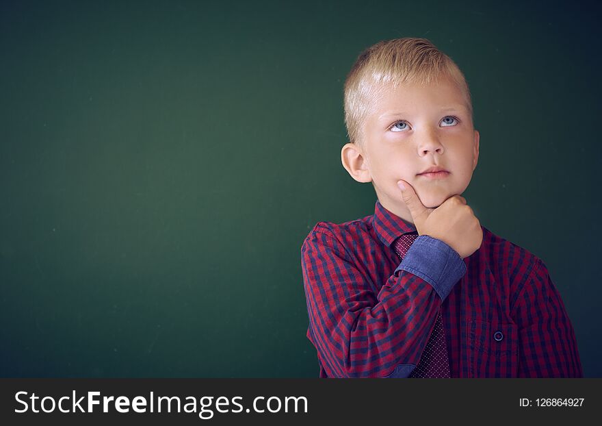 Closeup shot of schoolboy thinking with hand on chin isolated on blackboard. Portrait of pensive child thinking about