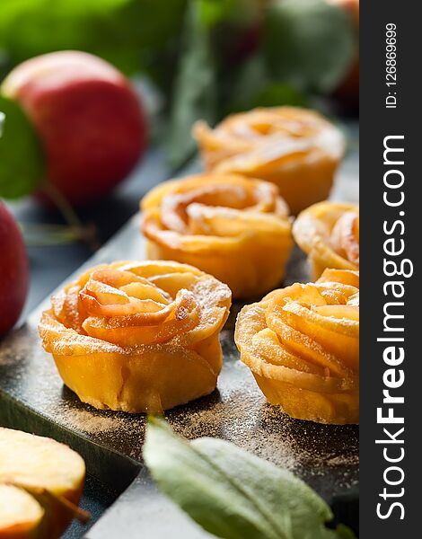 Apple Rose mini tarts with icing sugar on the stone cutting board.