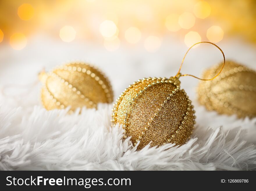 Gold Christmas baubles on white fur with gold sparkling background. Festive winter concept.
