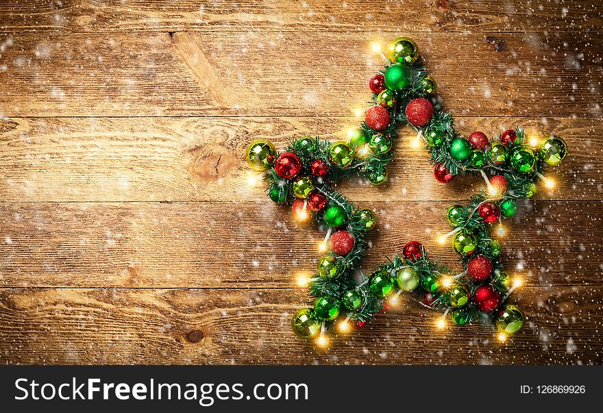 Decorative Christmas Star with colored baubles, christmas tree branches and lights on the rustic wooden board. Top view.