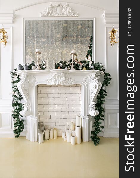 White fireplace decorated with candles and fir branches. Decorated Christmas tree. Classic apartments, morning in hotel.