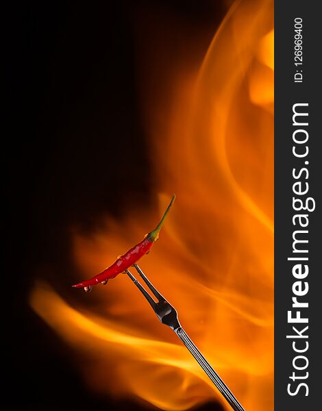 Chilli pepper on meat fork with flame behind on black background