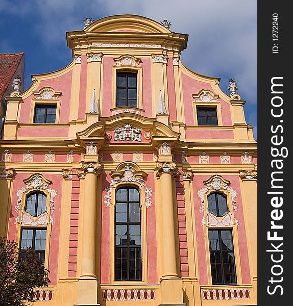 The picture shows an old, historic, baroque house facade in the city of Neuburg (Germany, Bavaria). The building is yellow and pink. There are ornaments around the windows. The image has a blue sky as background. The picture shows an old, historic, baroque house facade in the city of Neuburg (Germany, Bavaria). The building is yellow and pink. There are ornaments around the windows. The image has a blue sky as background.