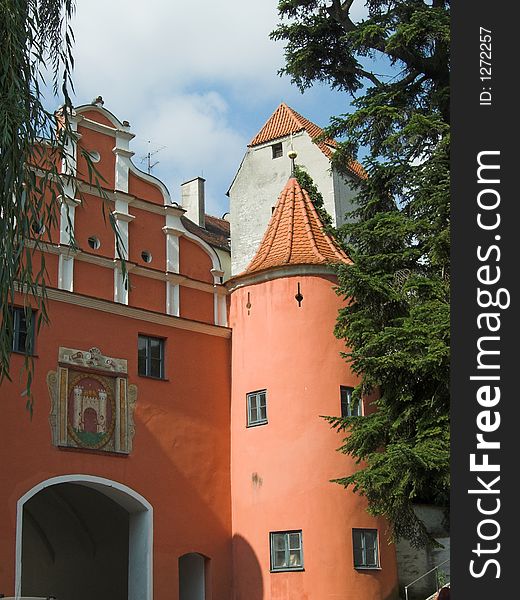 The picture shows a old, historic city gate in the town of Neuburg (Germany, Bavaria). It is a read building with an icon above the door. On the right side of the gate is a tower. The image is framed by two trees.