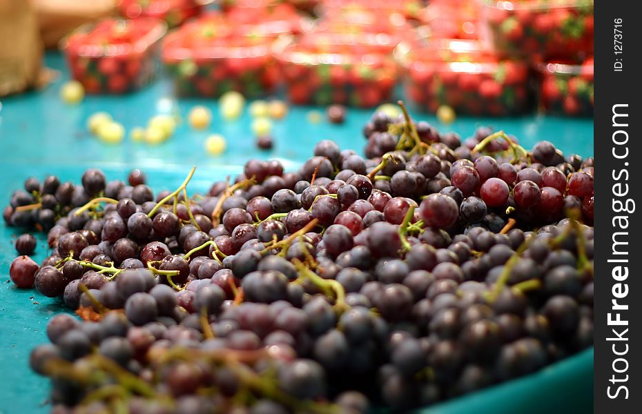 Ripe grapes bunches on blue display in the market, red strawberries on background.