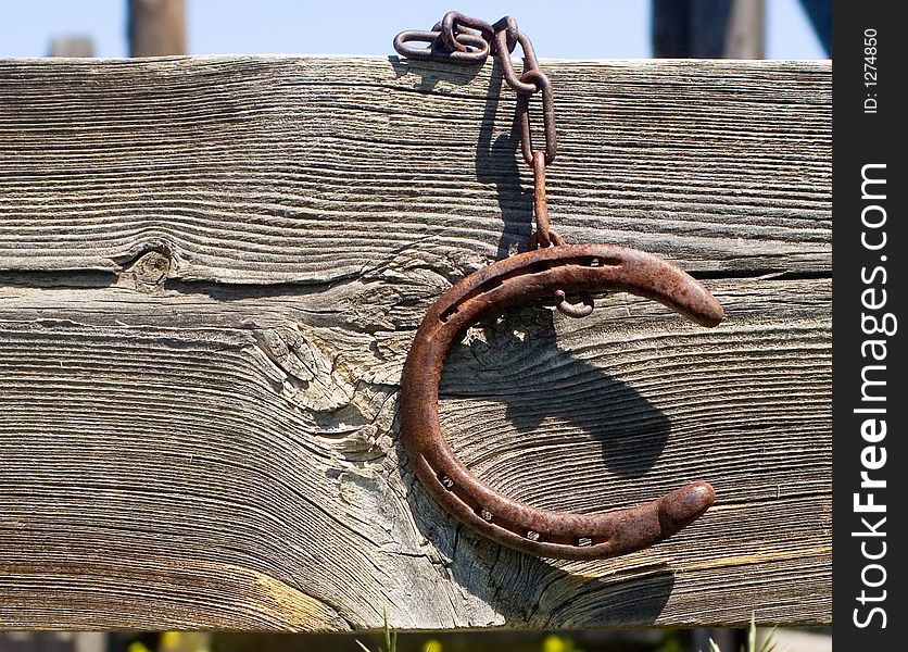 Rusty old horseshoe hanging by a rusty chain from a wooden fence. Rusty old horseshoe hanging by a rusty chain from a wooden fence