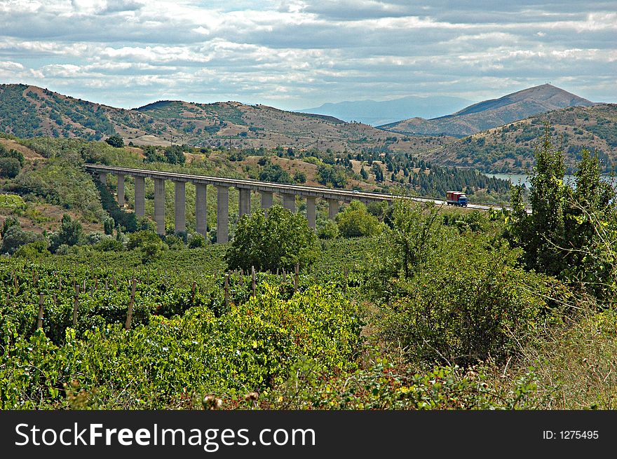 Macedonian landscape - road flyover towering over vast expanses of vineyards; hills and a lake in the background