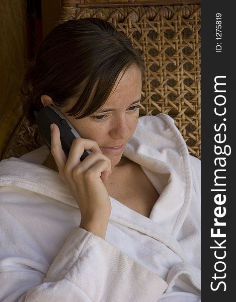 Girl relaxing in a wicker chair on the phone in her dressing gown. Girl relaxing in a wicker chair on the phone in her dressing gown