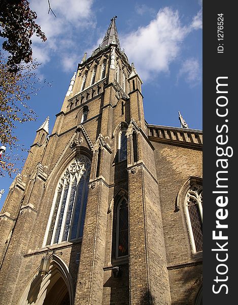 An upward view of a gothic architecture church with a spire (steeple) against a blue sky background. An upward view of a gothic architecture church with a spire (steeple) against a blue sky background