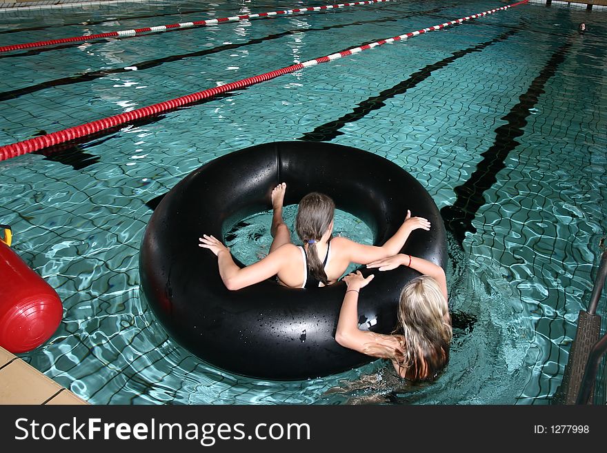 Indoor swimming pool fun, two girls playing with a big black buoy