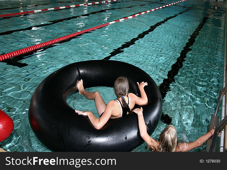 Indoor swimming pool fun, two girls playing with a big black buoy