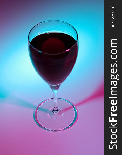 Glass of red wine lit by colour lights, focused on bottom.