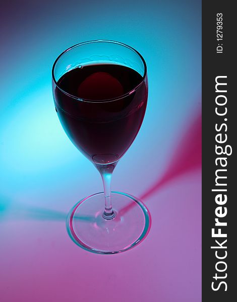 Glass of red wine lit by colour lights, focused on top.