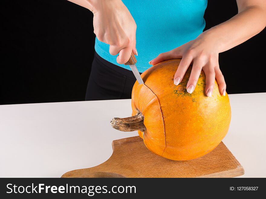 Young woman hand cuts big orange pumpkin on wooden board isolated on black background. Halloween and Thanksgiving day food concept. Close up. Young woman hand cuts big orange pumpkin on wooden board isolated on black background. Halloween and Thanksgiving day food concept. Close up