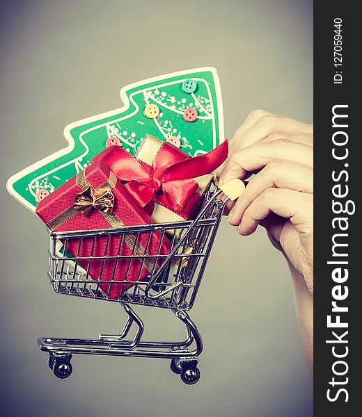 Xmas, seasonal sales, winter celebration concept. Woman hand holding shopping trolley cart basket with little christmas tree and gifts inside. Xmas, seasonal sales, winter celebration concept. Woman hand holding shopping trolley cart basket with little christmas tree and gifts inside.