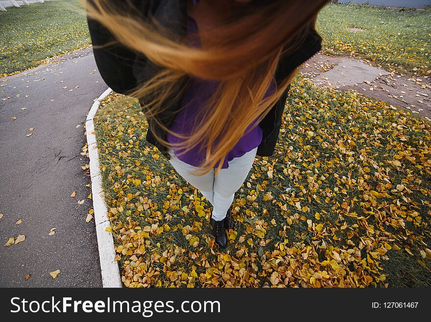 Woman legs in boots and blue jeas against a background yellow autumn leaves. Top view.