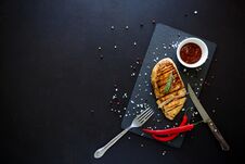 Grilled Chicken Fillets On Slate Plate With Rosemary, Pepper, Ketchup And Spices On Dark Wooden Background. Top View. Flat Lay. Stock Image Grilled Chicken Fillets On Slate Plate With Rosemary, Pepper, Ketchup And Spices On Dark Wooden Background. Top View. Flat Lay. Stock Image