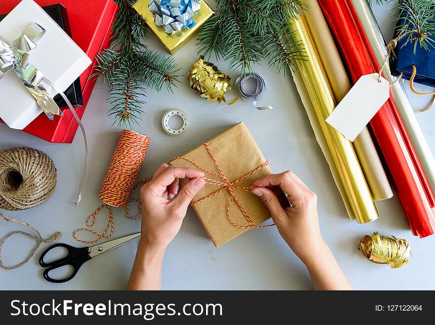 Woman`s hands decorate present box on gray wooden background. New Year and Christmas decorations concept