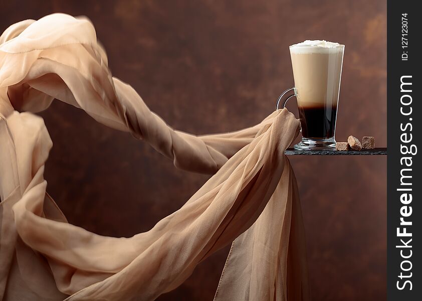 Coffee drink with cream and pieces of brown sugar on a brown background. Evolving in the wind chiffon scarf. Copy space for your text. Coffee drink with cream and pieces of brown sugar on a brown background. Evolving in the wind chiffon scarf. Copy space for your text.