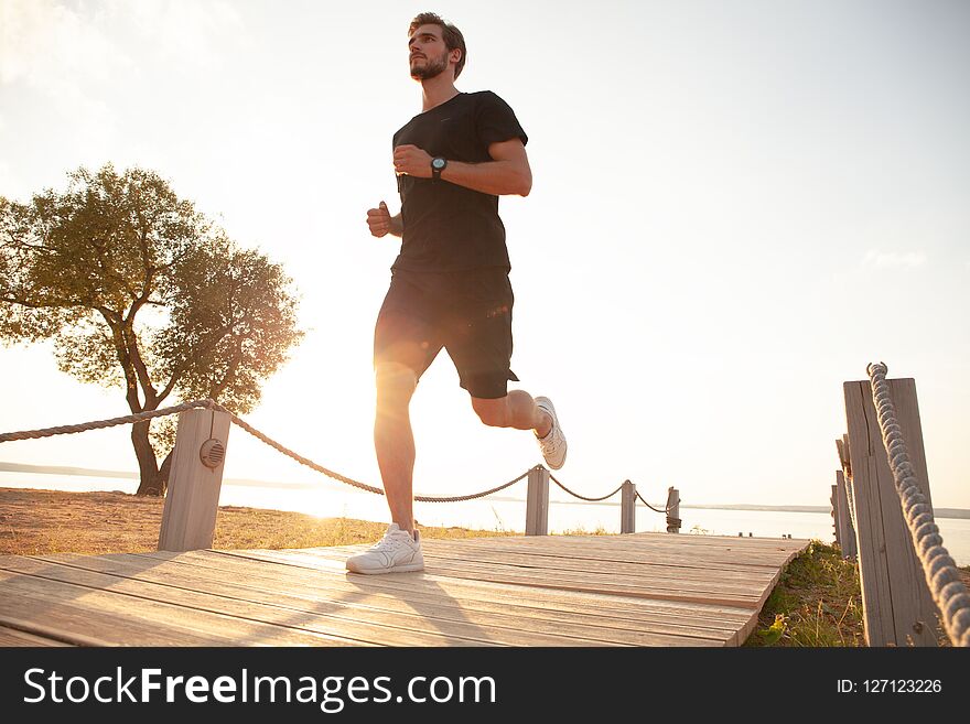 Full Length Shot Of Healthy Young Man Running On The Promenade. Male Runner Sprinting Outdoors