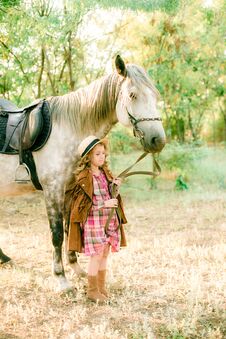A Nice Little Girl With Light Curly Hair In A Vintage Plaid Dress And A Straw Hat And A Gray Horse Stock Photo