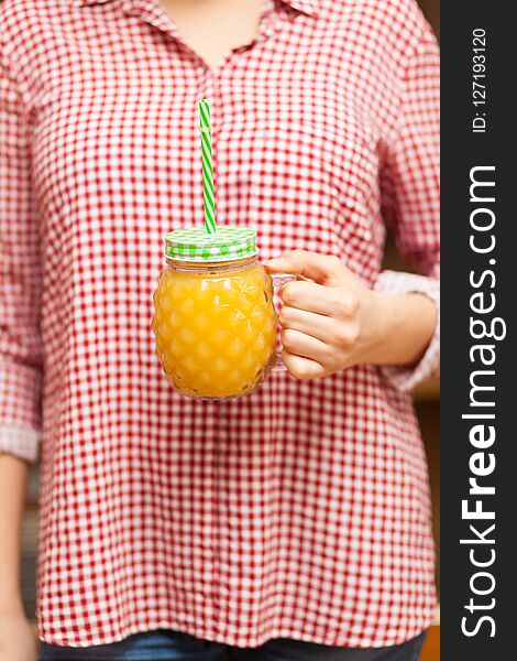 Girl in a red shirt holding a jar with juice in the form of pineapple
