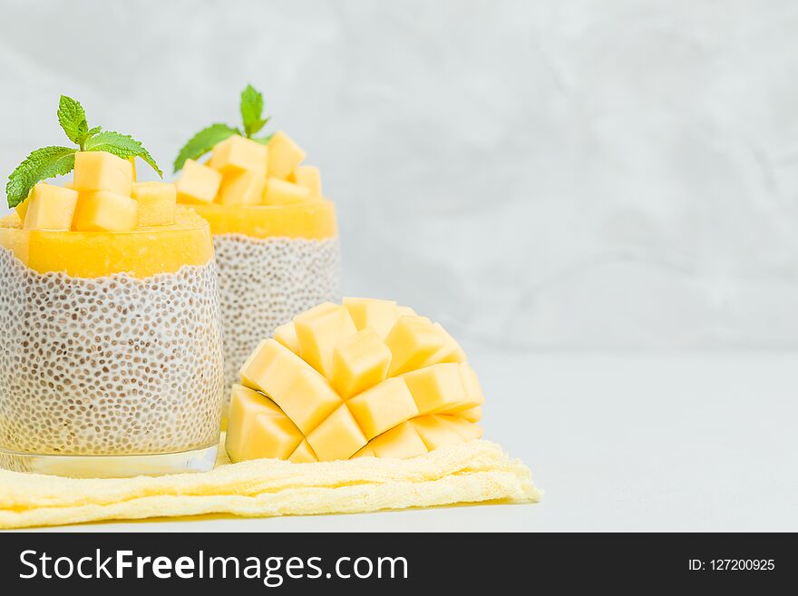 Chia seeds pudding with mango puree in beautiful glasses with green mint leaves and cut fresh ripe tropical fruit on light gray background - raw vegetarian sweet organic dessert. Chia seeds pudding with mango puree in beautiful glasses with green mint leaves and cut fresh ripe tropical fruit on light gray background - raw vegetarian sweet organic dessert.