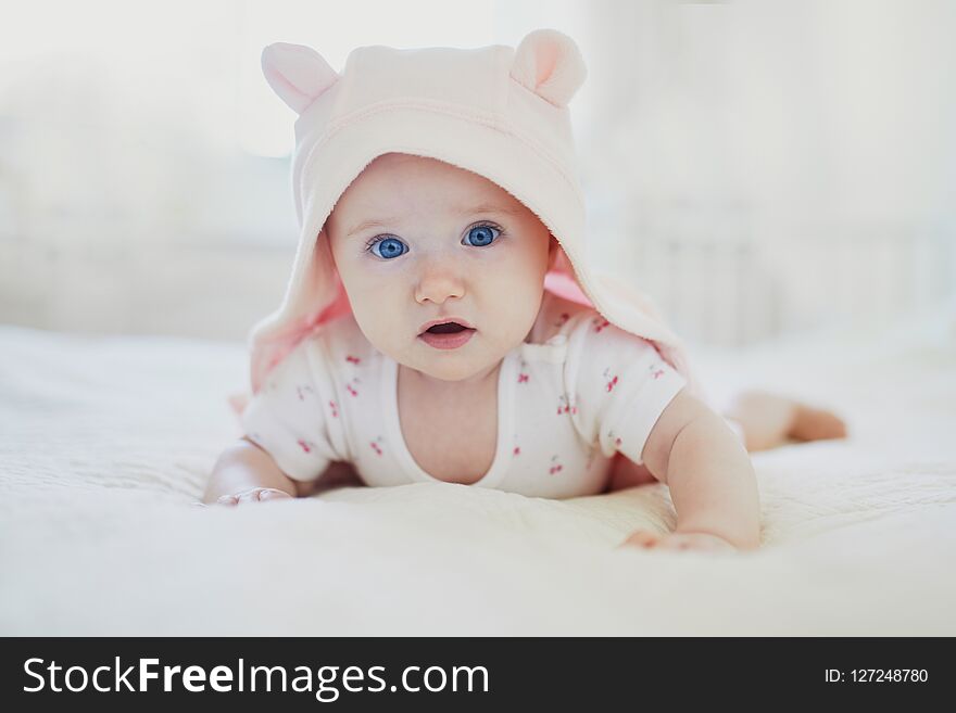Adorable baby girl in pink hoody crawling on bed