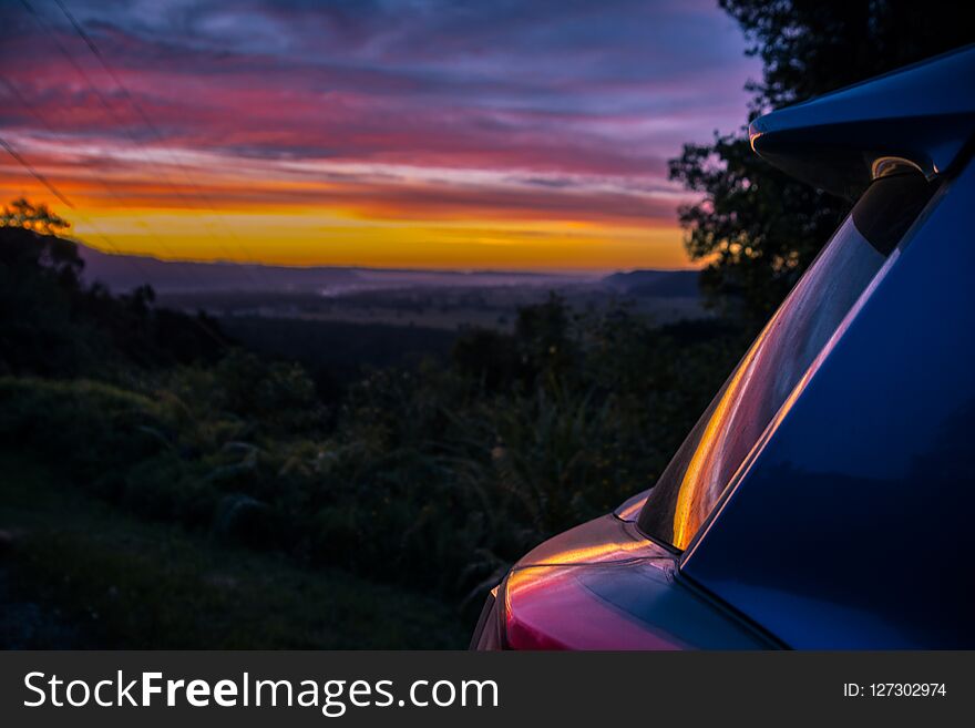 Piece of car reflecting colorful sunset sky on roadside of green spacious terrain of South Island. Piece of car reflecting colorful sunset sky on roadside of green spacious terrain of South Island