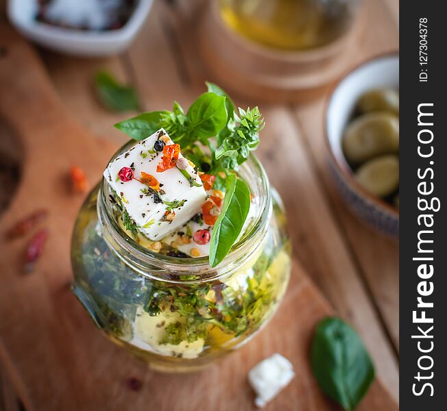Close-up of marinated feta cheese in olive oil, herbs and red pepper flakes on wooden background