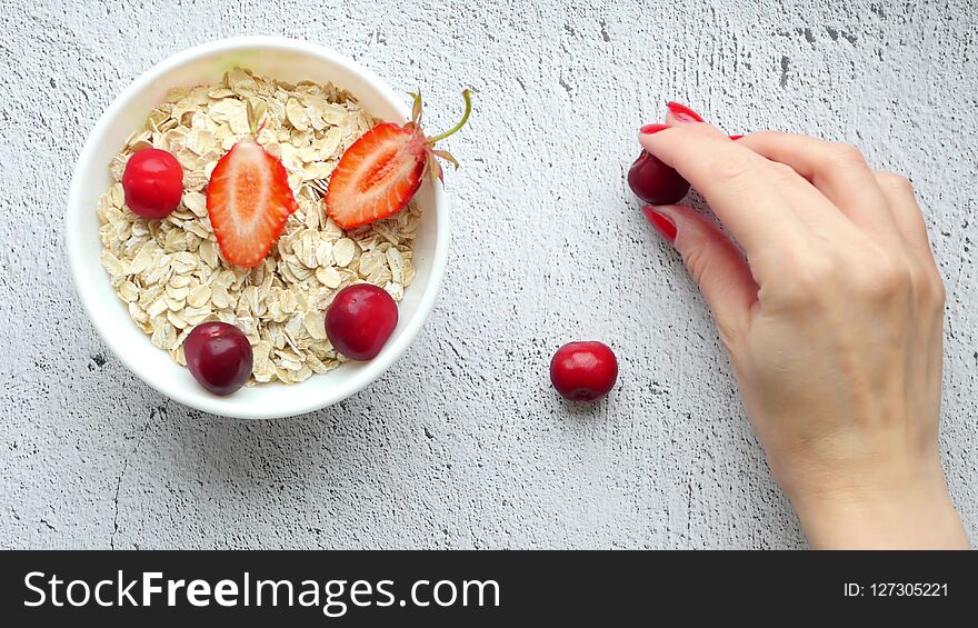 Beautiful female hands lay out on the table a composition of bright berries. Juicy red cherries on a white background. Bowl of oatmeal. Healthy breakfast. Proper nutrition. Fault on the table. 4k. Beautiful female hands lay out on the table a composition of bright berries. Juicy red cherries on a white background. Bowl of oatmeal. Healthy breakfast. Proper nutrition. Fault on the table. 4k