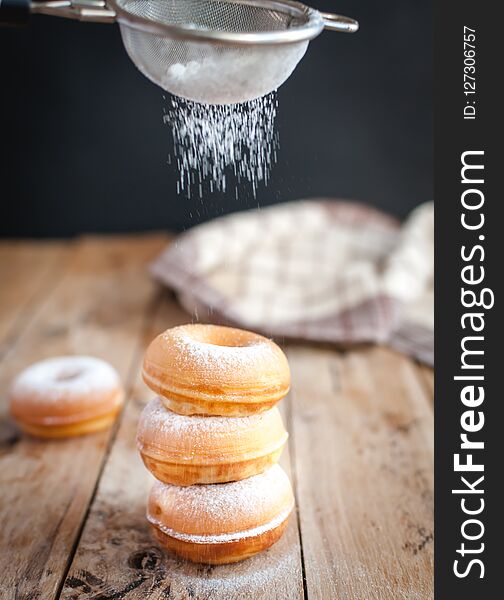 Sprinkling powdered sugar from above on stacked homemade donuts, on wooden background. Sprinkling powdered sugar from above on stacked homemade donuts, on wooden background.