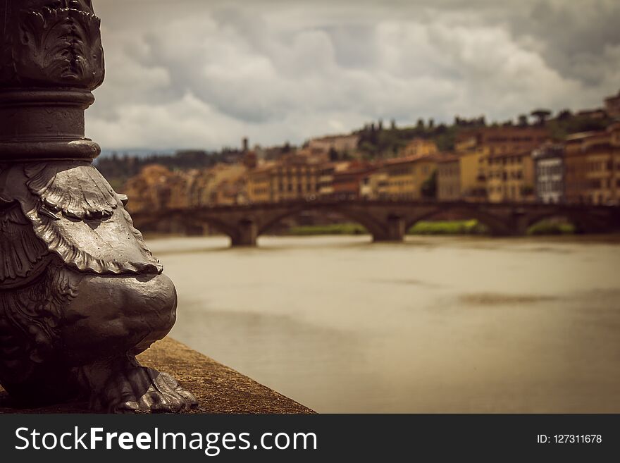 Portion of a luminaire next to the river. Panoramic view of the city of Florence unfocused. Storm clouds cover the sky.