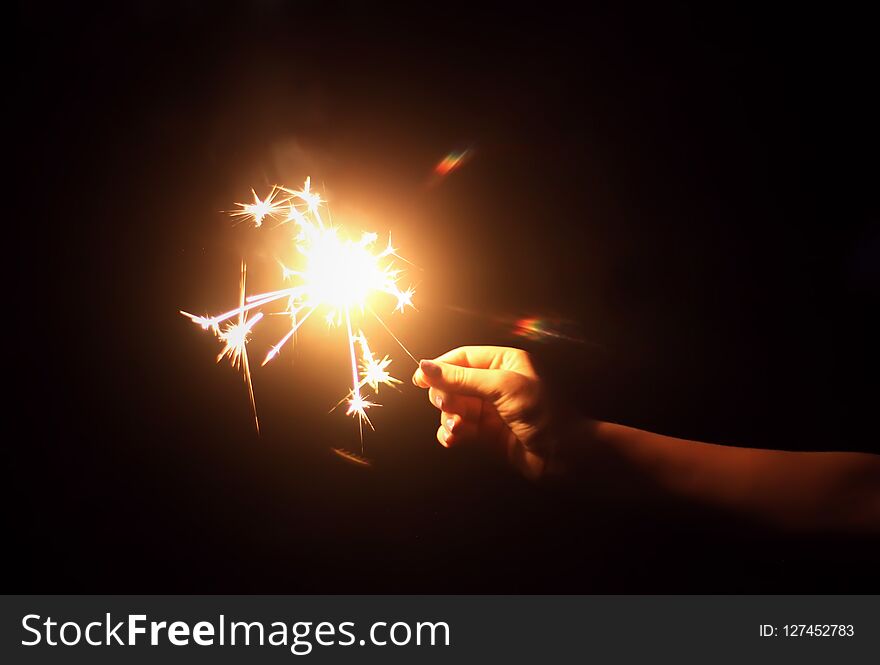 Female hand holding a burning sparkler on night darkness background.